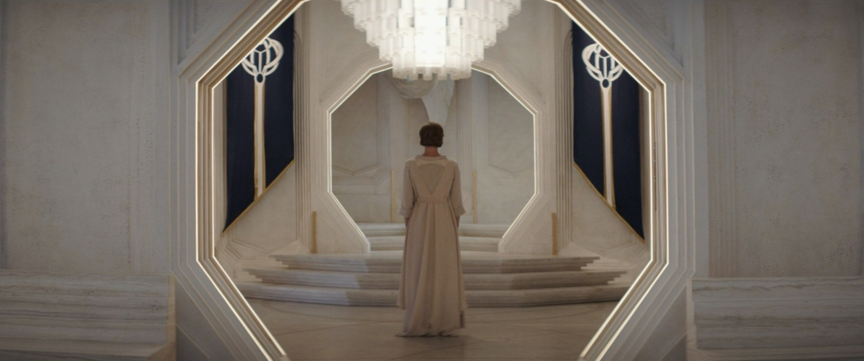 Mon Mothma, back turned to camera, standing in her home under a chandelier